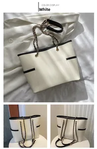 Detail of white contrast tote bag with black leather trim and golden metal chain strap
