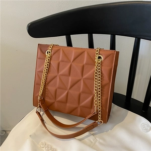 Sac bandoulière marron matelassé avec motif géométrique et chaîne dorée sur chaise