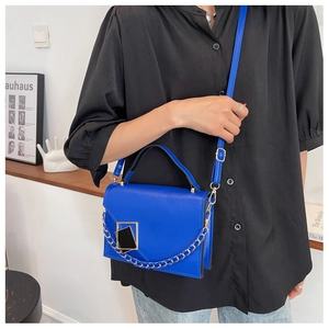 Detail of electric blue handbag with chunky chain strap worn by a model in a modern setting