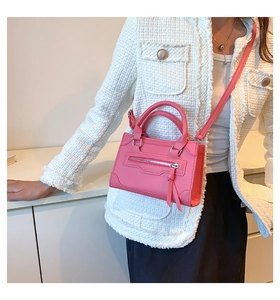 Close-up of pink mini crossbody bag with leather texture and fringe zipper detail on model