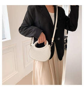 Détail d'un sac à main plissé blanc avec poignée ronde porté par un mannequin femme