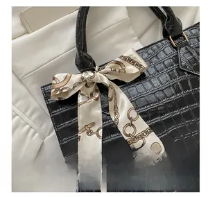 Close-up of black crocodile pattern handbag with elegant printed silk scarf detail