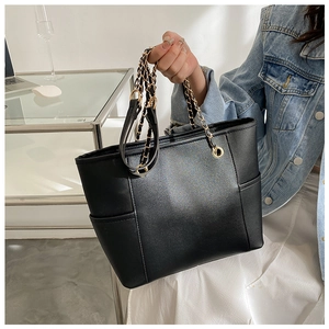 Detail of black faux leather tote bag with gold chain handles and side pockets