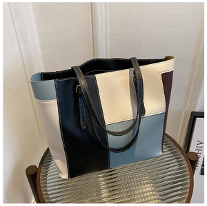Detail of color-block tote bag with white stitching and leather handles on glass table