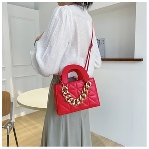 Detail of red quilted faux leather handbag with gold chain handle on shoulder