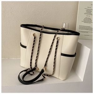 Detail of cream tote bag with black trim, side pocket and metal chain strap