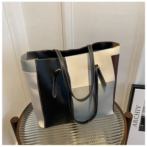 Detail of a color-block leather tote bag featuring contrast stitching on slim black handles