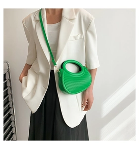 Sac croissant vert plissé avec poignée ronde porté par mannequin en costume blanc