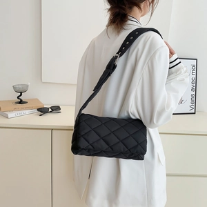 Sac bandoulière en nylon matelassé avec large sangle à œillets porté par un mannequin chic
