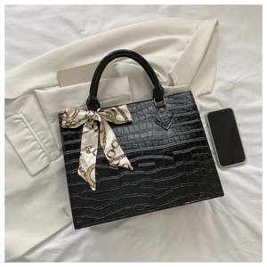 Close-up of black crocodile pattern handbag with silk scarf on white fabric