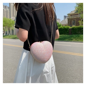 Detail of pink sequin heart-shaped crossbody bag with gold chain strap on street