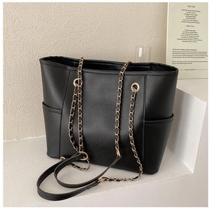 Close-up of black leather tote bag featuring gold chain straps and side slip pockets