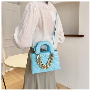 Close-up of light blue quilted square bag with gold chain strap and adjustable belt
