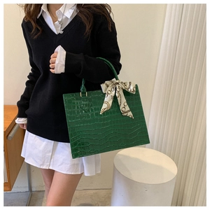 Detail view of a dark green crocodile texture tote bag with elegant silk scarf handle decoration