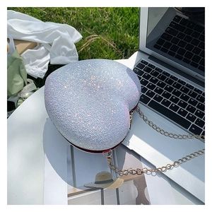 Detailed view of shimmering silver heart-shaped sequin bag with gold chain on grass