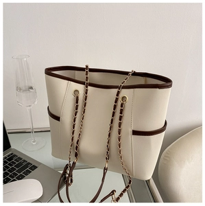 Detail of cream tote bag with brown trim featuring chain straps on an office desk