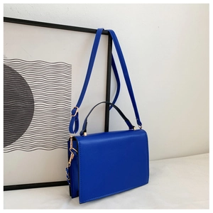 Detail of royal blue box bag with black handle and gold hardware in modern setup