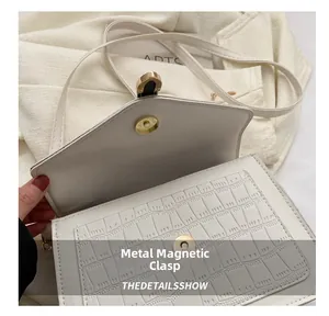 Detail showing high-quality metal magnetic snap closure and crocodile texture on white bag