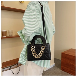 Close-up of black quilted crossbody bag with chunky gold chain handle on model