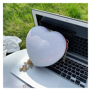 Detail of white sequined heart-shaped bag with gold chain strap on a laptop keyboard
