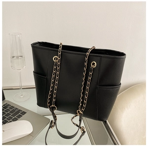Macro shot of large black tote bag with gold chain strap on a glass office desk