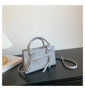 Detailed view of light grey top handle bag with front zipper pocket on a minimalist table