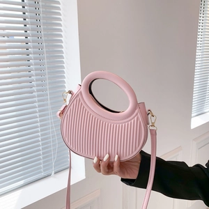Sac à main plissé rose avec poignée circulaire et bandoulière sous une lumière douce