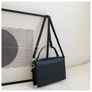 Detail of black square shoulder bag featuring gold hardware and curved top handle