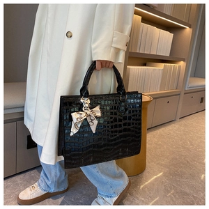 Detail of black faux crocodile leather tote bag with elegant silk scarf on handle