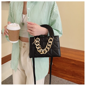 Detail of black quilted handbag with bold gold chunky chain strap on fashion model