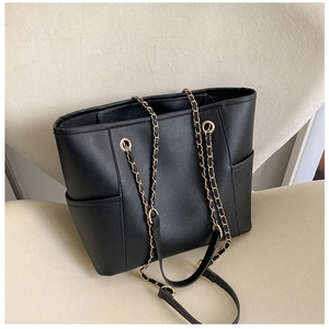 Detail of black tote bag with gold chain strap and side pockets on a chair