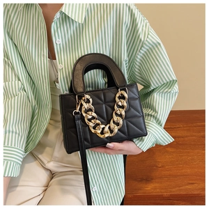 Close-up of black quilted shoulder bag with chunky gold chain and rigid top handle