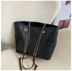 Detail of black tote bag with gold metal chain strap and functional side pockets