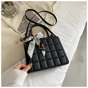 Gros plan d'un sac à main noir matelassé avec anse en foulard de soie sur literie blanche