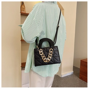 Detail view of black quilted crossbody bag with stylish gold chain and top handle strap