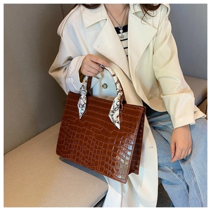 Detail of dark brown croc-embossed tote bag with a decorative floral silk scarf handle