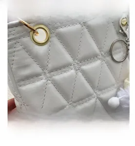 Macro view of white quilted PU leather handbag featuring metal eyelets and a plush pompom