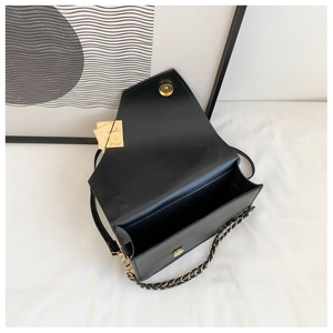 Detail view of black leather crossbody bag with magnetic closure and gold chain strap
