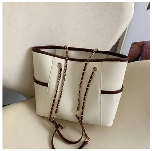 Detail view of cream tote bag with brown trim and gold chain strap on soft background