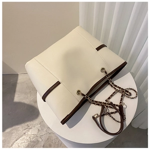 Detail of a white tote bag with brown trim and gold chain strap on a white stand