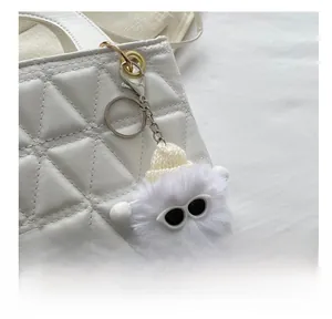 Detail of a white faux fur ball charm with sunglasses attached to a quilted handbag