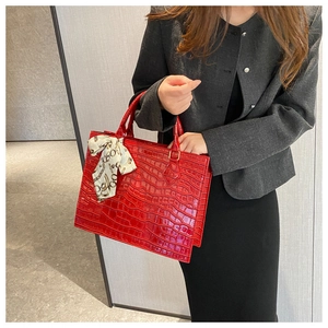 Detail of red croc-embossed tote bag with decorative silk scarf and gold chain pattern