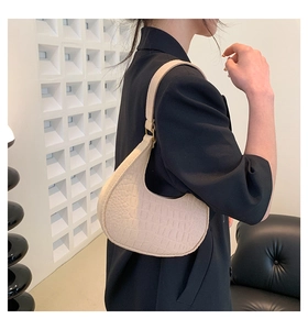 Detail of light beige crocodile embossed crescent bag with gold buckle on shoulder
