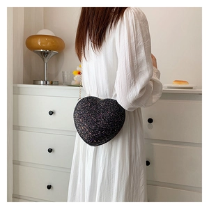 Detail of a black heart-shaped crossbody bag with shimmering sequins and gold chain strap