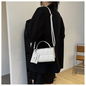 Detailed view of white quilted shoulder bag with matching mini pouch on a black blazer