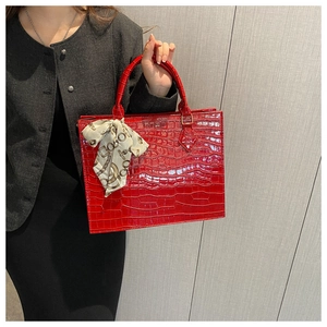 Detail of red croc-embossed leather tote bag with a silk scarf tied on the top handle