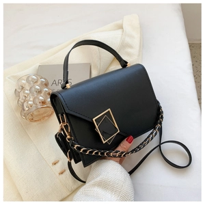 Detail of black leather handbag with square gold buckle and chain accent on white fabric