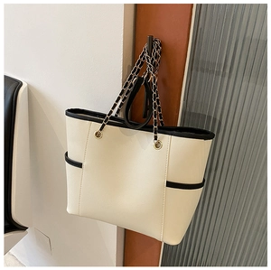 Detail of a large cream and black tote bag with gold chain strap hanging on a door