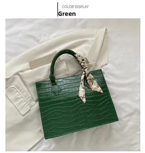 Detail of green crocodile pattern handbag with silk scarf handle on white background