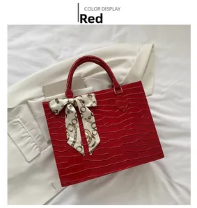 Detail of red crocodile pattern handbag with gold hardware and silk scarf decoration